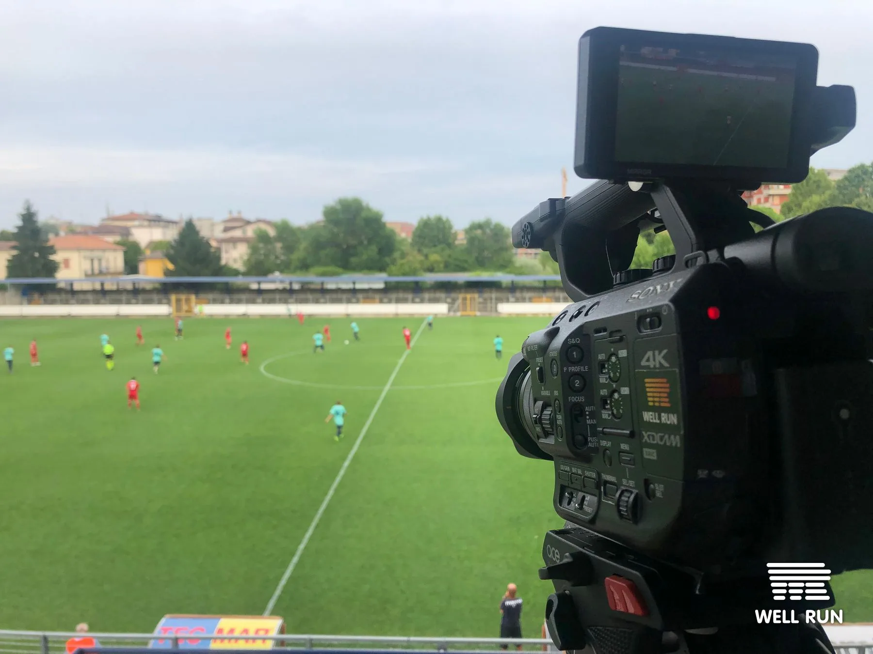 Sony 4K XDCAM camera on tripod overlooking football pitch with players in red and cyan kits, Crema Italy