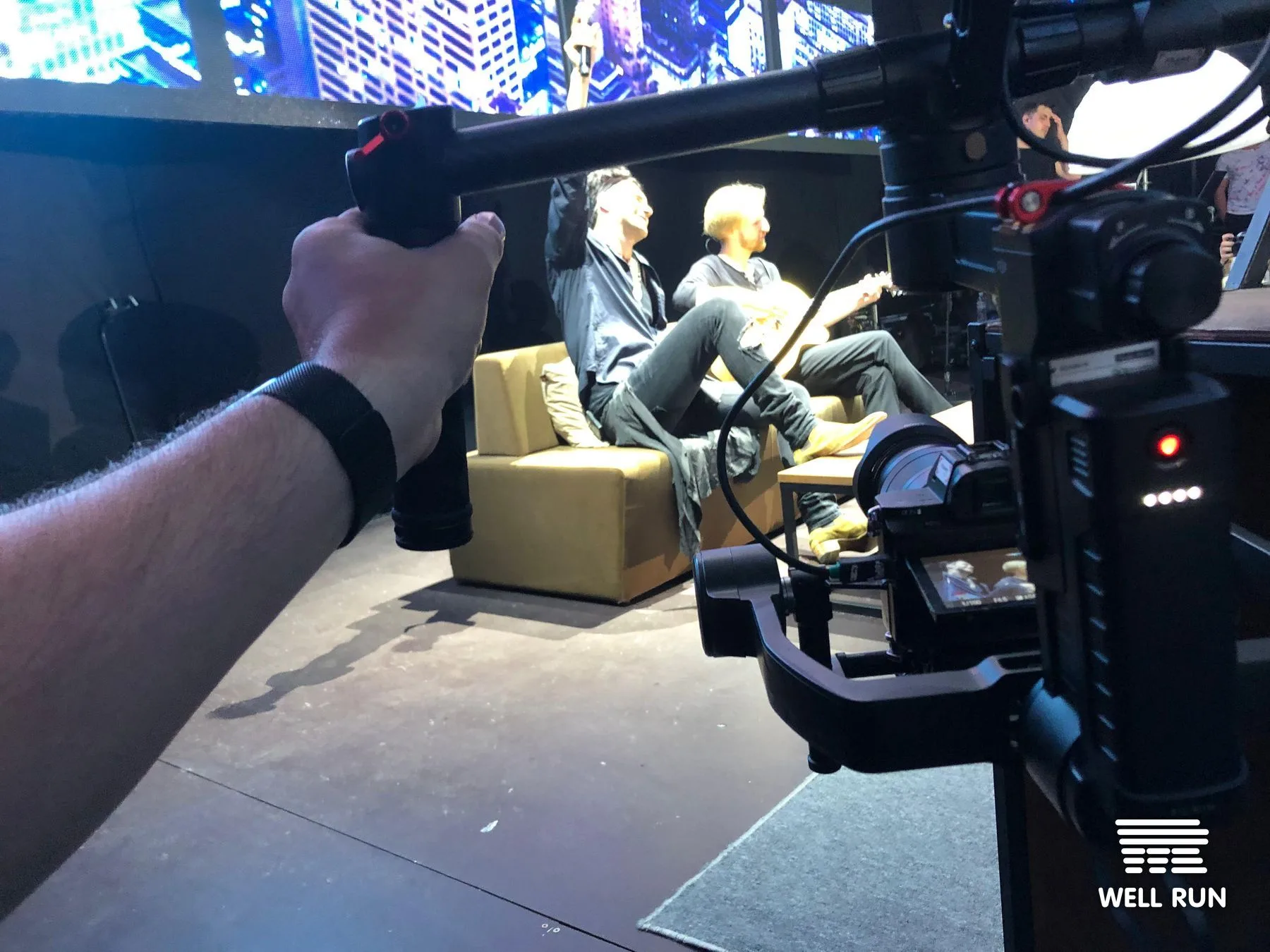 Camera operator holds gimbal rig filming two people seated on stage at Dan Balan concert, Odessa