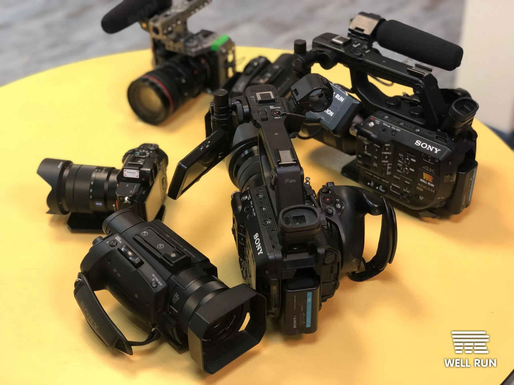 Multiple Sony video cameras and lenses laid out on a yellow table before a concert shoot