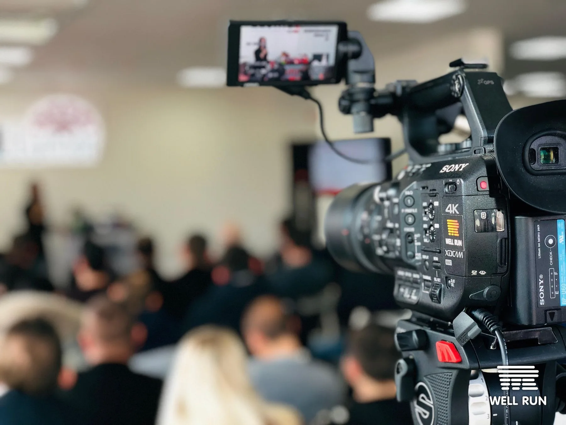 Sony 4K XDCAM camera on rig filming blurred seated audience at indoor Llumar event, Kyiv