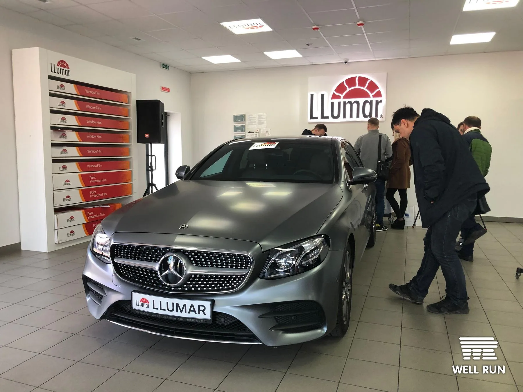 Silver Mercedes sedan on display inside LLumar Kyiv showroom, guests examining the car