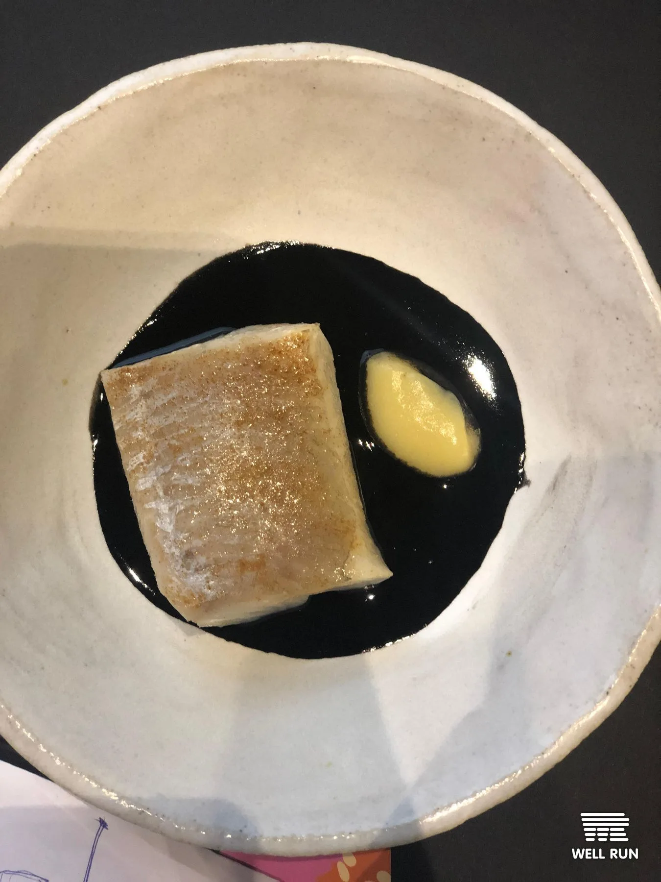 Seared fish fillet on black squid ink sauce with aioli, served in a rustic ceramic bowl
