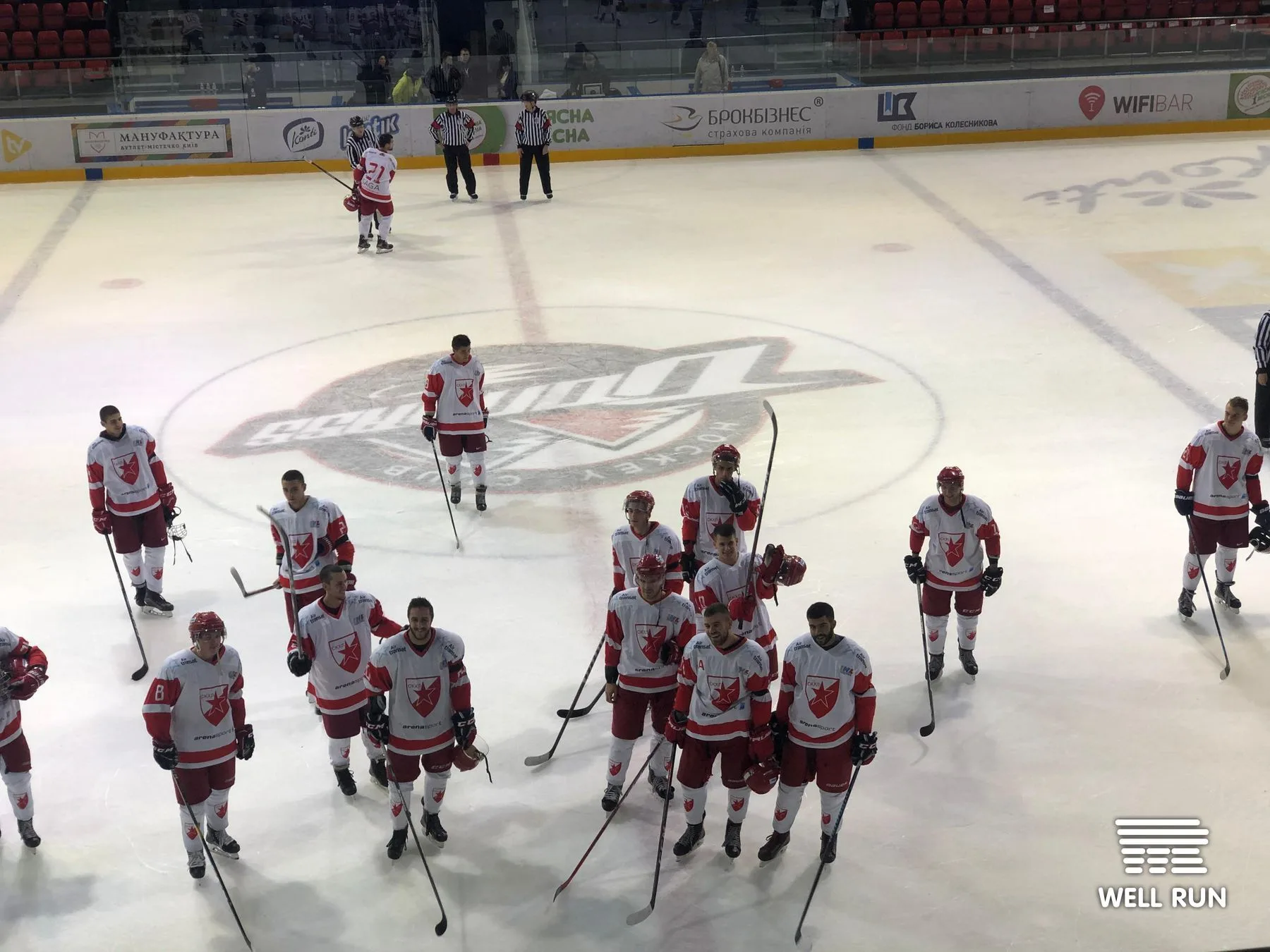 Hockey players in red and white jerseys stand on ice at Brovary Arena, Ukraine