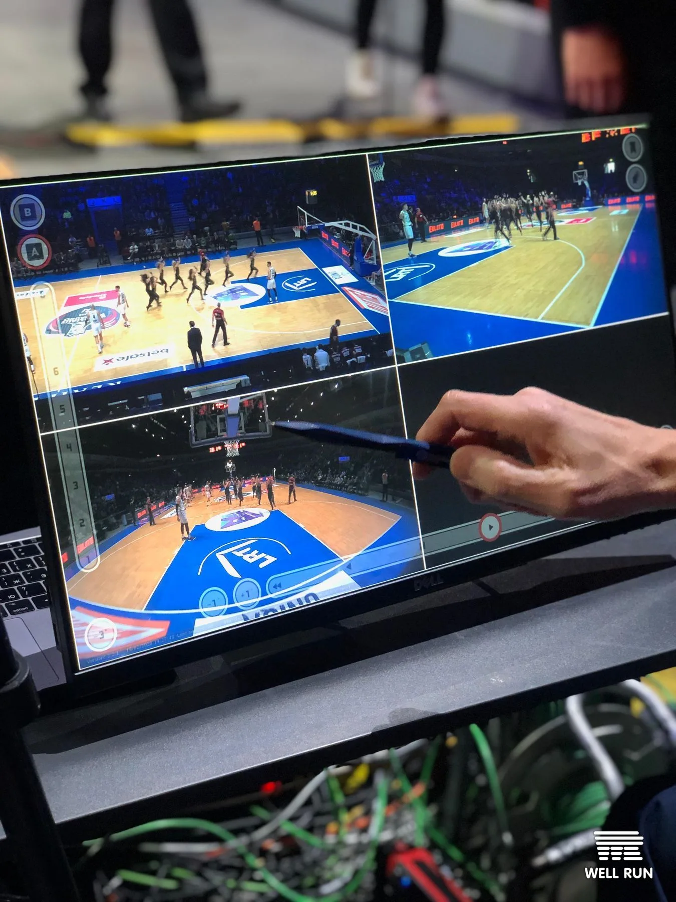 Hand holding stylus navigating four-angle replay on Dell touchscreen monitor at basketball officials table — frame 5