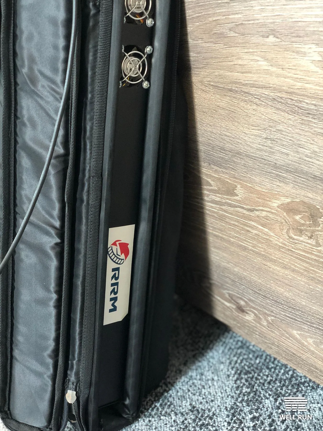 RRM mini-PC unit inside open black padded travel case, dual cooling fans visible, RRM logo label on side panel — frame 5
