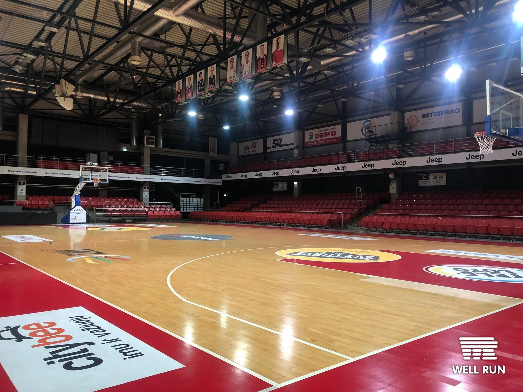 Empty basketball court with red seats, sponsor hoardings, and two hoops at LKL venue Vilnius — frame 7