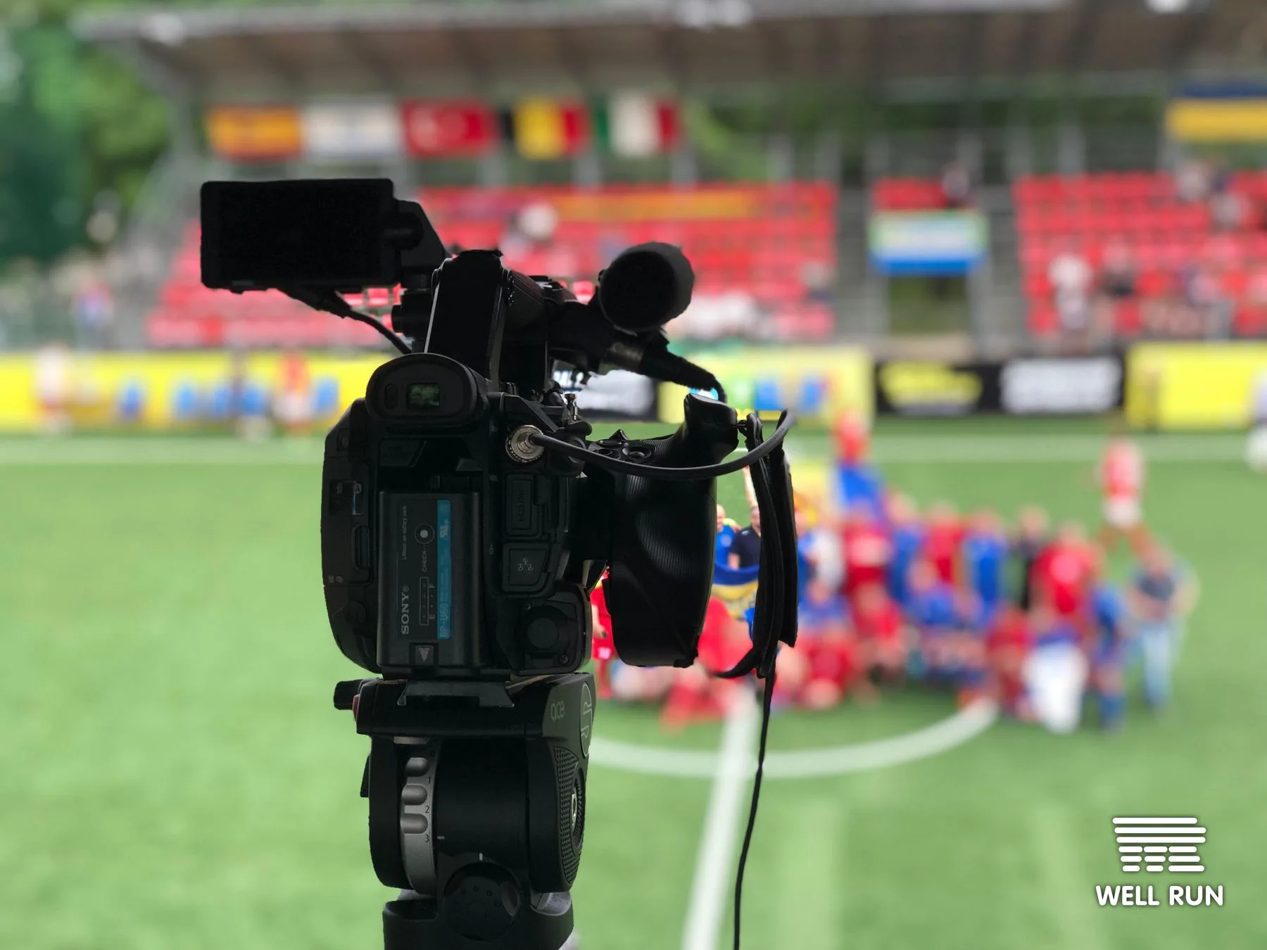 Sony broadcast camera on tripod at Hydropark Arena, players gathered on 6x6 pitch behind — frame 1