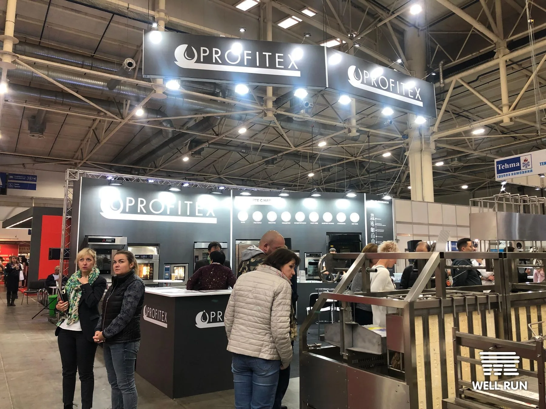 Attendees at Profitex exhibition stand displaying commercial ovens inside large expo hall — frame 1