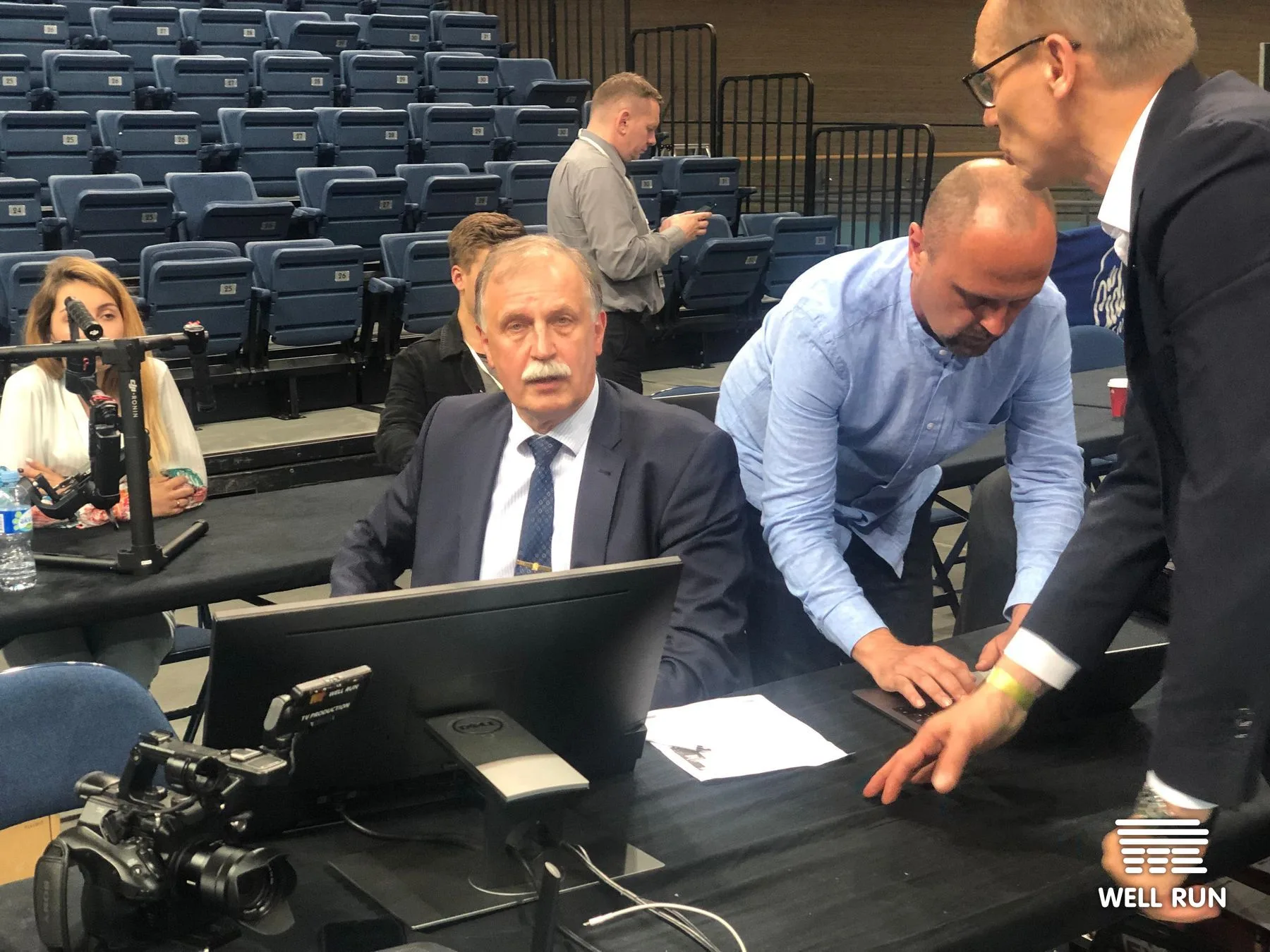 Three men review RRM system on Dell monitor courtside at empty Vilnius LKL arena
