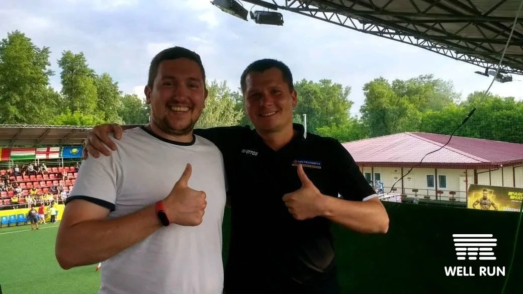 Andrew Kuznezov and Sergei Ruzhutskiy smiling thumbs-up at Hydropark Arena outdoor football venue Kyiv