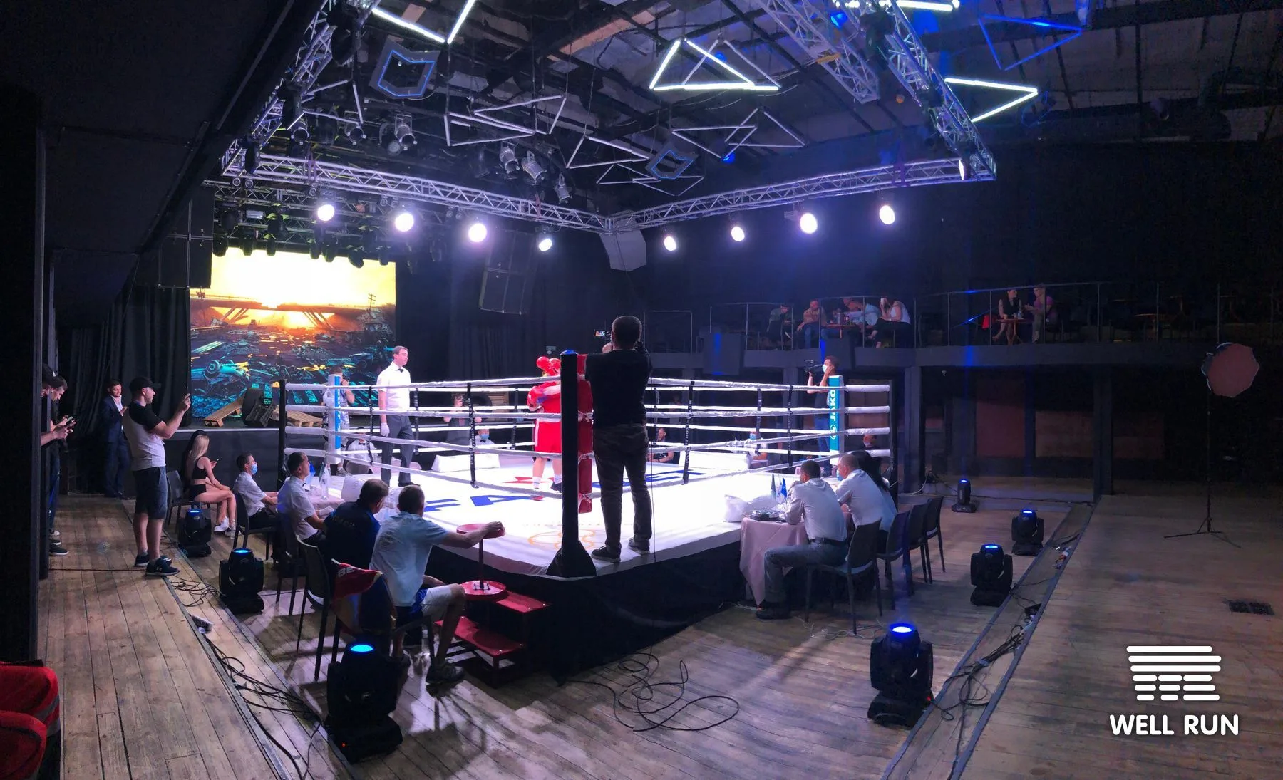 Boxing ring at Club Atlas Kyiv with two fighters, referee, ringside judges, and camera operator — frame 1