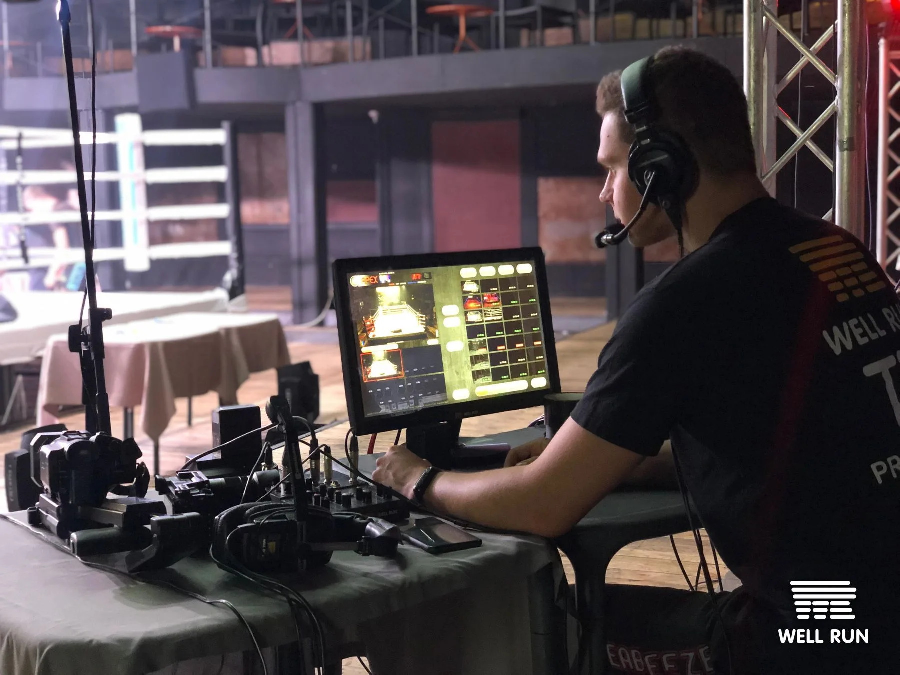 Technician wearing headset monitors multi-camera feed on screen at ringside production desk, Club Atlas Kyiv